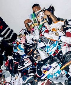 a man sitting on top of a pile of shoes and holding a book in his hands