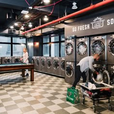 two people are doing laundry in front of washers and dryers at the same time