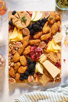 an assortment of cheeses, fruit and crackers on a cutting board next to wine glasses