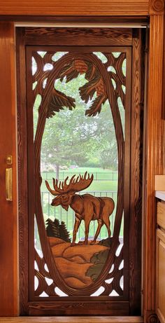 a wooden door with an image of a moose and pine trees on the glass panel