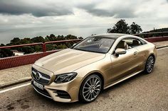 a gold mercedes benz coupe parked on the side of the road with dark clouds in the background