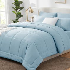 a bed with blue comforter and pillows in a room next to a plant on the floor