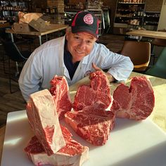 a man sitting at a table with raw meat in front of him and pointing to the camera