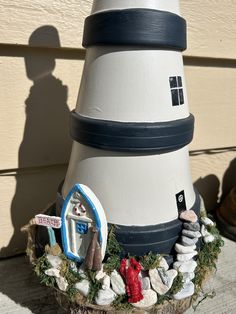 a white and black lighthouse on top of a wooden table next to a building with a red door