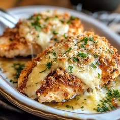 two pieces of chicken covered in cheese and parmesan on a plate with a fork