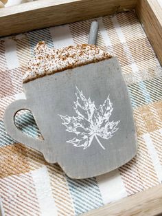 a cup of coffee on a plaid tablecloth with a maple leaf drawn on it