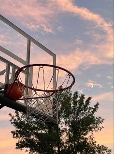 a basketball hoop with the sun setting in the sky behind it and some trees below