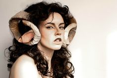 a woman with horns on her head is posing for the camera and has long curly hair