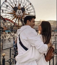 a man and woman standing next to each other in front of a ferris wheel at an amusement park