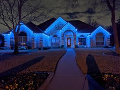 a house with blue lights in the front yard and trees on either side of it