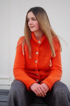 a woman in an orange cardigan sitting on a bench