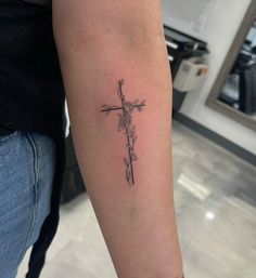 a cross tattoo on the left arm with flowers and leaves around it, in black ink