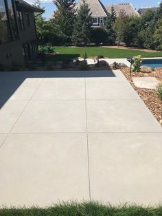 an empty concrete patio in front of a house with a swimming pool and green grass