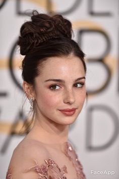 a beautiful young lady wearing a pink dress with a bun in her hair and earrings