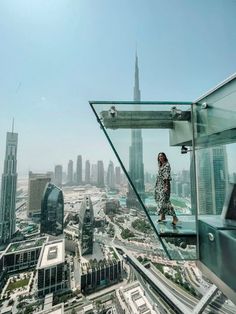 a woman standing on the edge of a glass walkway in front of a cityscape