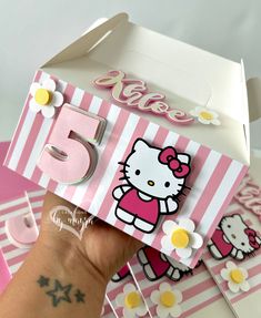 a hand holding up a hello kitty card in front of a box with flowers on it