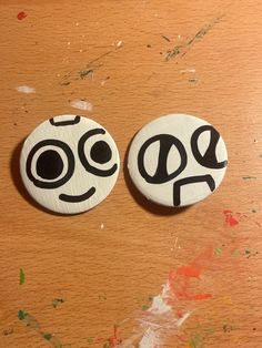 two buttons with faces drawn on them sitting on a wooden table next to each other