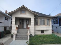 a small white house sitting on the side of a street next to two houses with grass in front of it