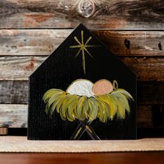 a painting of a baby jesus in a manger scene on a black wooden house