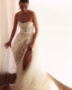 a woman in a wedding dress leaning against a window with her leg on the floor