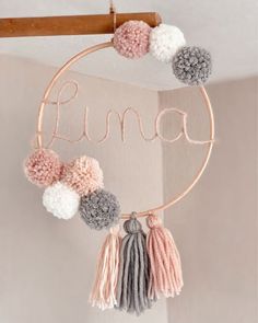 a pink, grey and white pom - pom dream catcher hanging on a wall