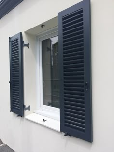 an open window with blue shutters on the side of a white wall and sidewalk