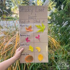 a person holding up a sign with leaves on it in front of some grass and trees