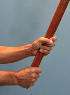 a man holding onto a wooden stick with one hand and the other arm extended up