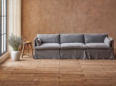 a couch sitting in front of a window next to a table with a potted plant on it