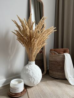 a white vase with some dry grass in it next to a mirror and other items