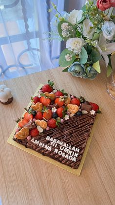 a chocolate cake with strawberries and other toppings on a table next to flowers