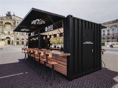 an outdoor bar with wooden tables and stools in the middle of a city square