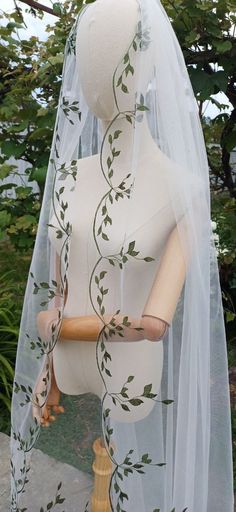 a white mannequin wearing a veil with green leaves on it