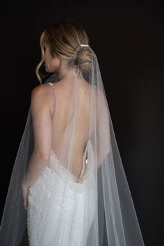 the back of a bride's wedding dress with a veil on her head and shoulders