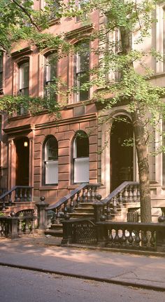 an old building with stairs leading up to the front door and trees growing on the sidewalk