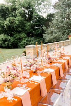 a long table is set up with orange linens and place settings for the guests