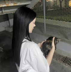 a woman holding a small cat in her hands while standing next to a metal fence