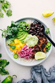 a white bowl filled with rice, black beans and veggies next to lime wedges