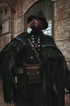 a man dressed in black with large feathers on his head and wearing a long coat