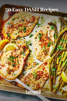 fish and asparagus on a baking sheet with lemon wedges