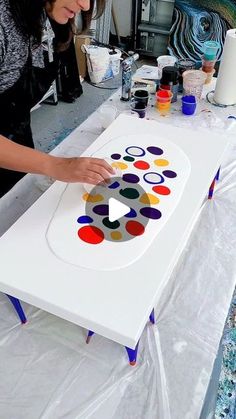 a woman is making an art project with circles on a large white board and paint