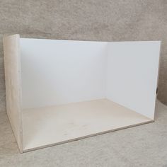 an empty white cardboard box sitting on top of a table next to a gray wall