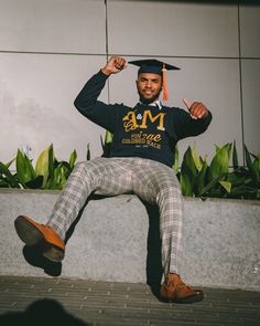 a man sitting on the ground wearing a graduation cap and plaid pants with his legs crossed