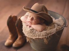 a baby wearing a cowboy hat sleeping in a bucket with his hands under his chin