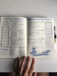 an open notebook with a hand holding the pages in front of it on top of a table