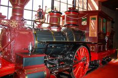 an old fashioned train is on display in a museum room with red carpet and large windows