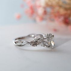 a diamond ring sitting on top of a white surface with pink flowers in the background