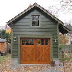 a garage with two doors and windows in the middle of an area that has fallen leaves on the ground