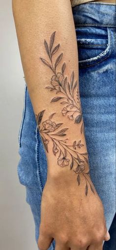 a woman's arm with a tattoo on it that has leaves and flowers on it