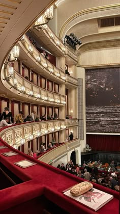 an auditorium filled with lots of people sitting on red seats and looking up at the stage